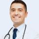 David Villar, doctor sonriente con bata blanca y estetoscopio alrededor del cuello, viste camisa de rayas y corbata azul.