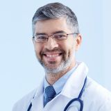 Emerson Anderson, doctor sonriente con gafas, bata blanca y estetoscopio alrededor del cuello.